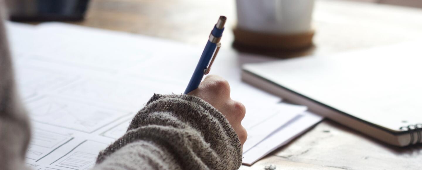 Someone writing at a desk with a cup of coffee