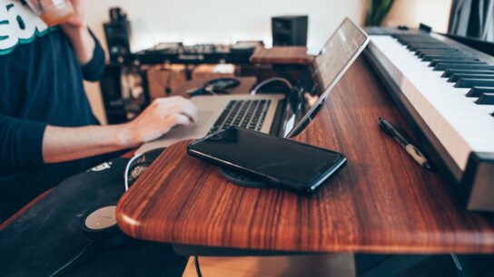 Music student sat a desk with a laptop and keyboard in front of them